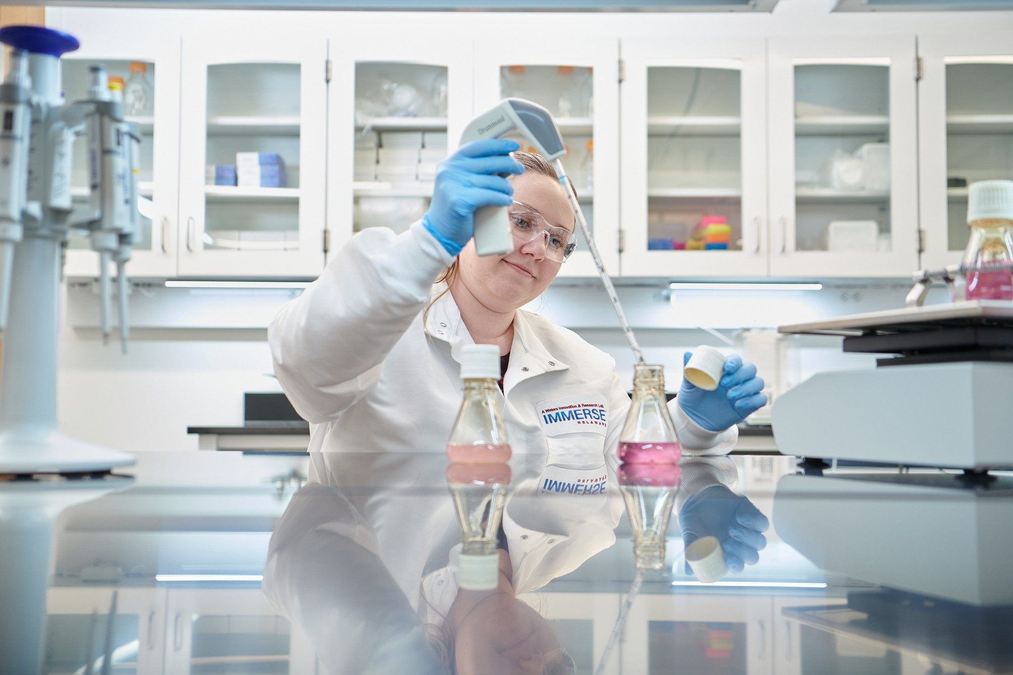 Female scientist at the Immerse Delaware laboratory using a large instrument to work with liquid in a flask