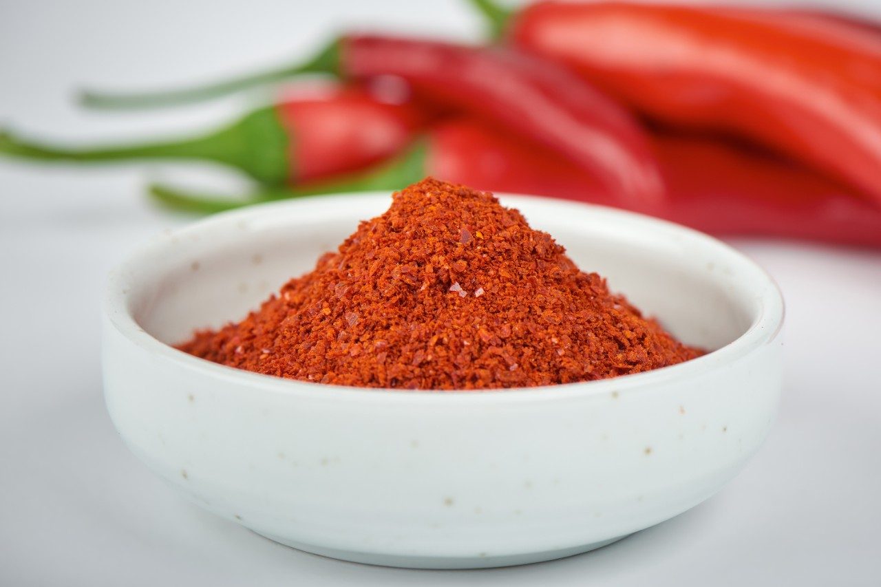 Korean chili pepper powder in a bowl with chili peppers in background