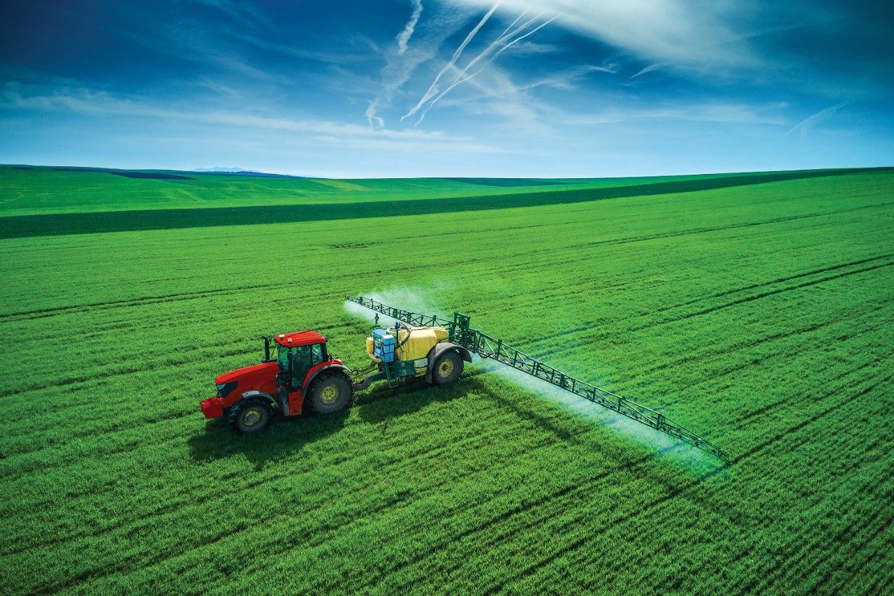 Tractor plowing and spraying pesticides in field