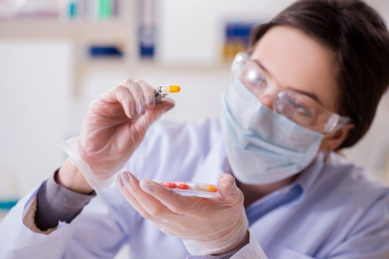 Lab assistant in PPE examining pills